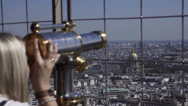 Woman on viewpoint of Eiffel tower looking at cityscape through coin binocular, Paris