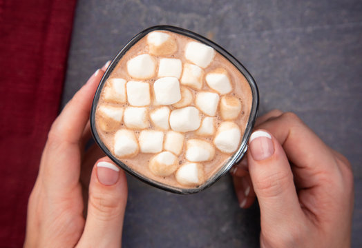 Woman Holding a Cup of Hot Chocolate with Marshmallows on a Dark Table