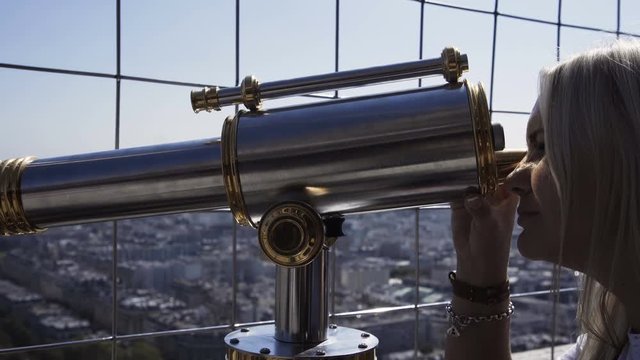 Woman on viewpoint of Eiffel tower looking at cityscape through coin binocular, Paris
