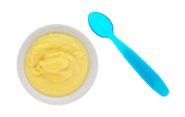 Top view of homemade banana cream pudding in a small bowl with a blue plastic spoon to the side isolated on a white background.