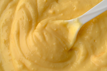 Top close view of fresh creamy homemade banana cream pudding with a white plastic spoon in the food illuminated with window light.