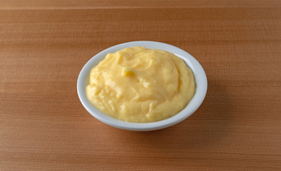 Side view of homemade banana cream pudding in a white dish atop a wood table illuminated with window light.