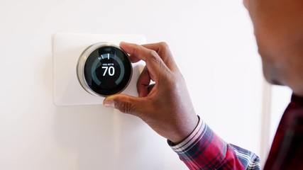 Close Up Of Man Setting Smart Heating Thermostat At Home