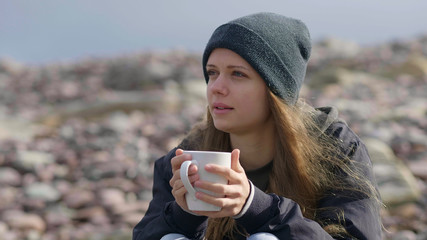 Beautiful girl with a cup of coffee sitting at the waterfront