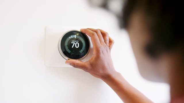Close Up Of Woman Setting Smart Heating Thermostat At Home