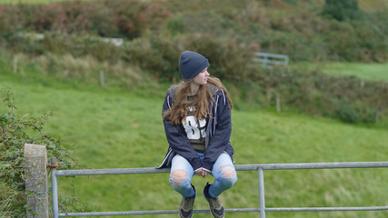 Beautiful girl sits on a gate and enjoys the surroundings