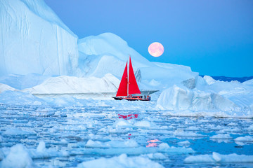 Little red sailboat cruising among floating icebergs in Disko Bay glacier during midnight sun season of polar summer. Ilulissat, Greenland. - obrazy, fototapety, plakaty