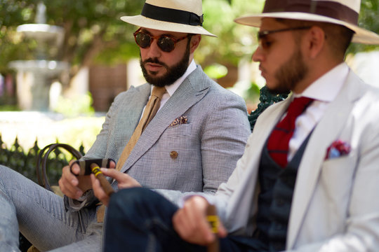 Two stylish men cutting open a cigar