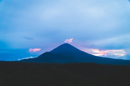 Mount Agung spewing a small cloud of toxic gases, lit from behind by a red sunrise