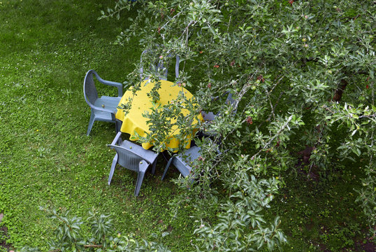 Table with yellow tablecloth and chairs in a garden, seen from above