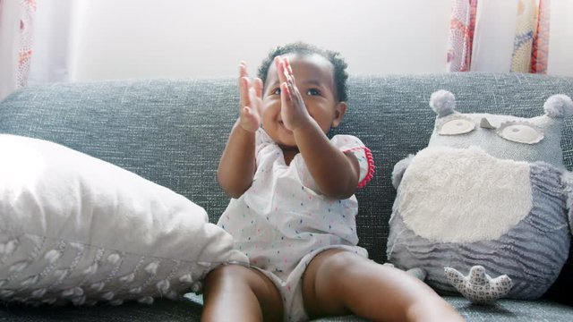 Baby Girl Sitting On Sofa And Clapping At Home