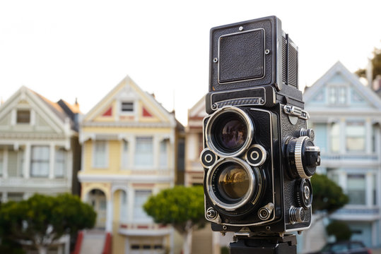 Twin-lens reflex camera on a tripod in front of a row of homes