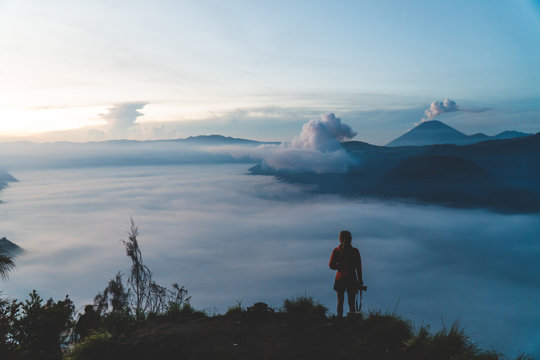 A young woman standing on the edge of a giant cliff, overlooking Mount Bromo and the Tengger Crater