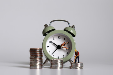 A concept of working hours and income disparity. A miniature person with an alarm clock and a pile of coins.