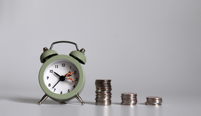 Concept of working time and salary. A miniature person with an alarm clock and a pile of coins.