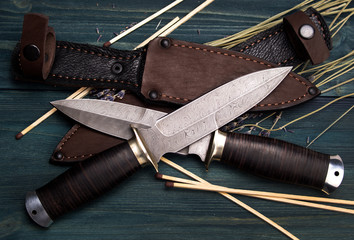 Damascus hunting knives with leather sheath on a vintage wooden background
