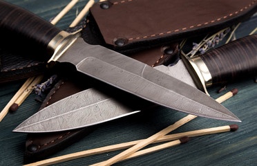 Damascus hunting knives with leather sheath on a vintage wooden background
