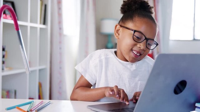 Young Girl Wearing Glasses Sitting At Desk In Bedroom Using Laptop Computer