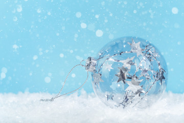 One crystal glass Christmas bauble with silver tinsel inside on a white snow with blue background,...