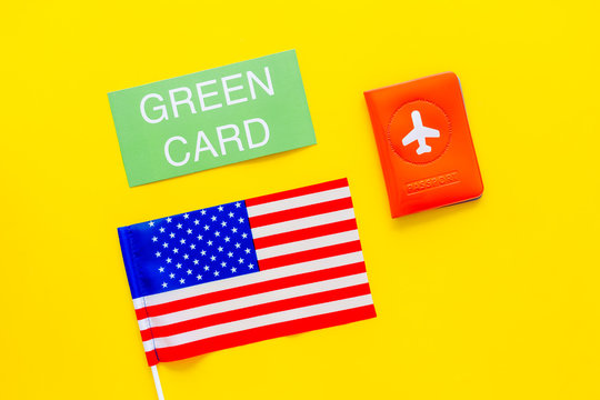 United States of America permanent resident cards. Immigration concept. Text green card near passport cover and US flag top view on yellow background