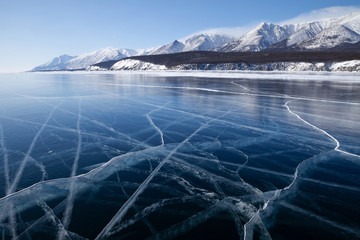 Beautiful cracks pattern on glossy smooth surface of frozen lake Baikal, scenic winter landscape or background with blue ice open space and mountains covered with snow