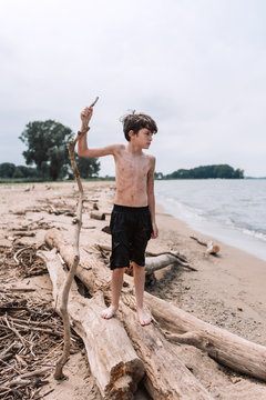 Shirtless boy standing with stick on wooden log