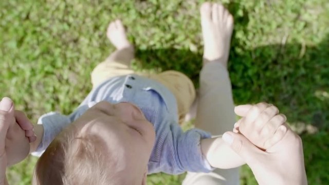 POV of woman holding hands of cute toddler walking on green grass in park on summer day