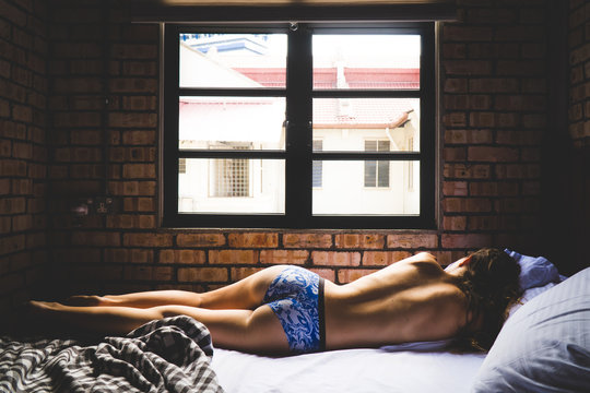 A young woman laying uncovered on a bed in only underwear