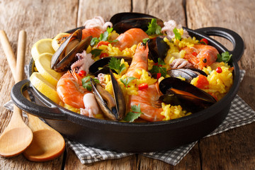 Homemade freshly prepared paella with king prawns, mussels, fish, and baby octopus served in a pan on a wooden table. horizontal