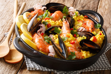 Spanish spicy paella seafood with king prawns, mussels, fish, and baby octopus closeup on wooden background. horizontal