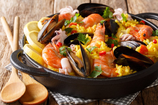 Paella seafood with king prawns, mussels, fish, and baby octopus served in a pan on a wooden table. horizontal