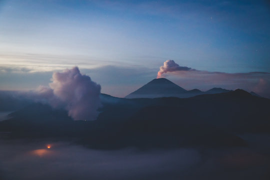 An erupting volcano glowing in the distance at dawn