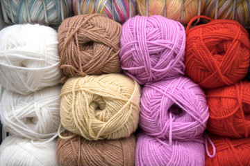 A number of multicolored woolen skeins arranged in rows on a store shelf, yarn texture