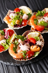 Gourmet seafood salad of shrimp, baby octopus, mussels, squids and scallops in sea shells close-up. vertical