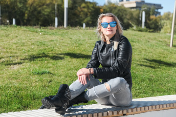 The woman sits on a bench in jeans, a jacket