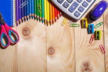 Pencils in rainbow color wave and other stuff lying on a light wooden background