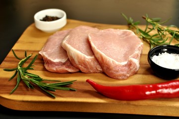 Raw fresh uncooked sliced pork fillet dish with rosemary, pepper, salt, red chili pepper, on wooden board and black background. Top side view