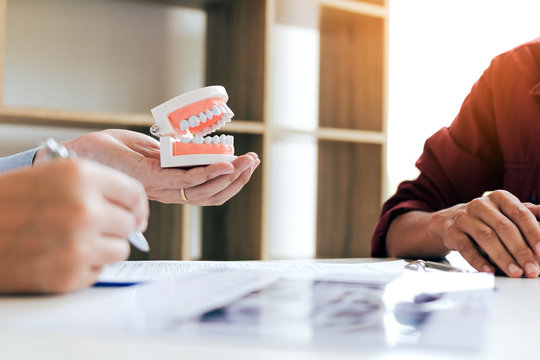 Confident dentist man holding a dentures with talking senior patient at office room.