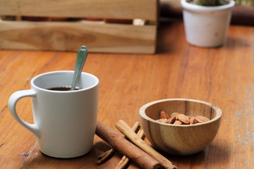 Breakfast hot black coffee in white cup, cinnamon, almond nut in wooden bowl and cactus pot plant on wood table