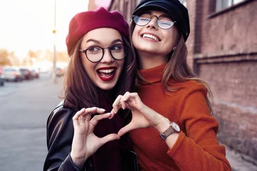 Foto op Plexiglas Outdoors fashion portrait young pretty best girls friends in friendly hug. Walking at the city. Posing at the street. Wearing stylish outerwear and hats. Bright make up. Positive emotions. © opolja