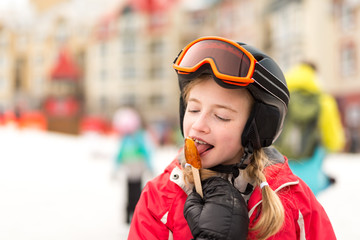 Girl wearing goggles and snow helmet enjoys maple syrup lollipop