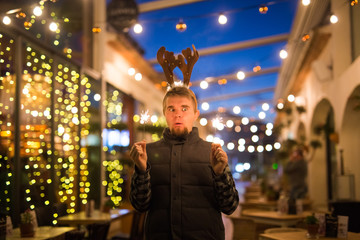 Obraz premium People, holidays and Christmas concept - young funny man in christmas deer costume with bengals light outdoors