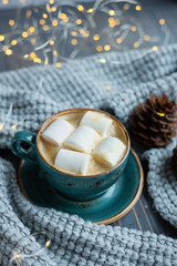 Obraz na płótnie Canvas Cup of coffee, marshmallow, warm knitted sweater on wooden background. Warm lights. Cozy winter morning. Lifestyle concept. Selective focus.