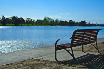 Empty bench facing lake with blue sky and blue water
