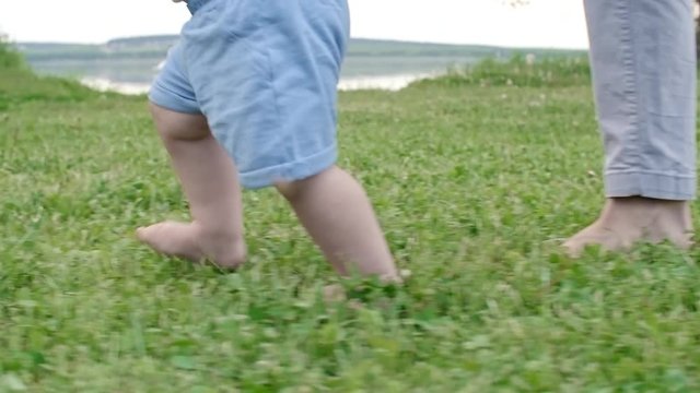 Tracking with low-section of legs of toddler and mother walking on green grass