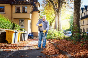 Senior sweeping autumn leaves.