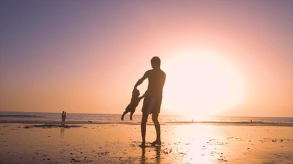 Ultra slow motion - silhouette of father and son playing together in the beach at sunset