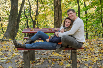 Couple in love sitting on a bench in the autumn park among the yellow fallen leaves