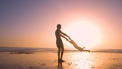 Ultra slow motion - silhouette of father and son playing together in the beach at sunset