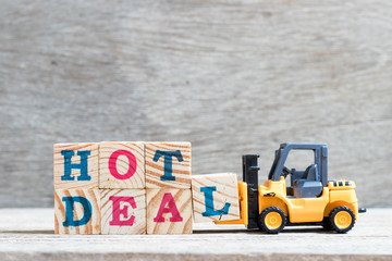 Toy forklift hold letter block L to complete word hot deal on wood background